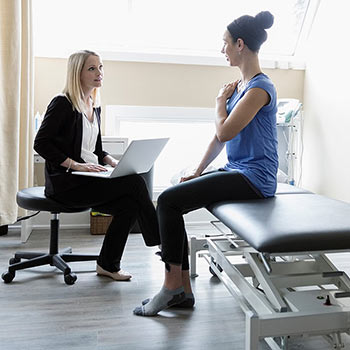 Physical therapist using CONNECT rehab EMR software while talking to patient